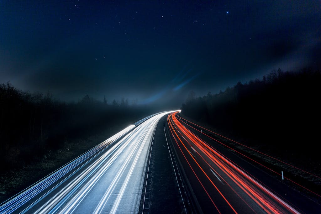 Long exposure night shot capturing stunning red and white light trails on a highway under a starry sky.